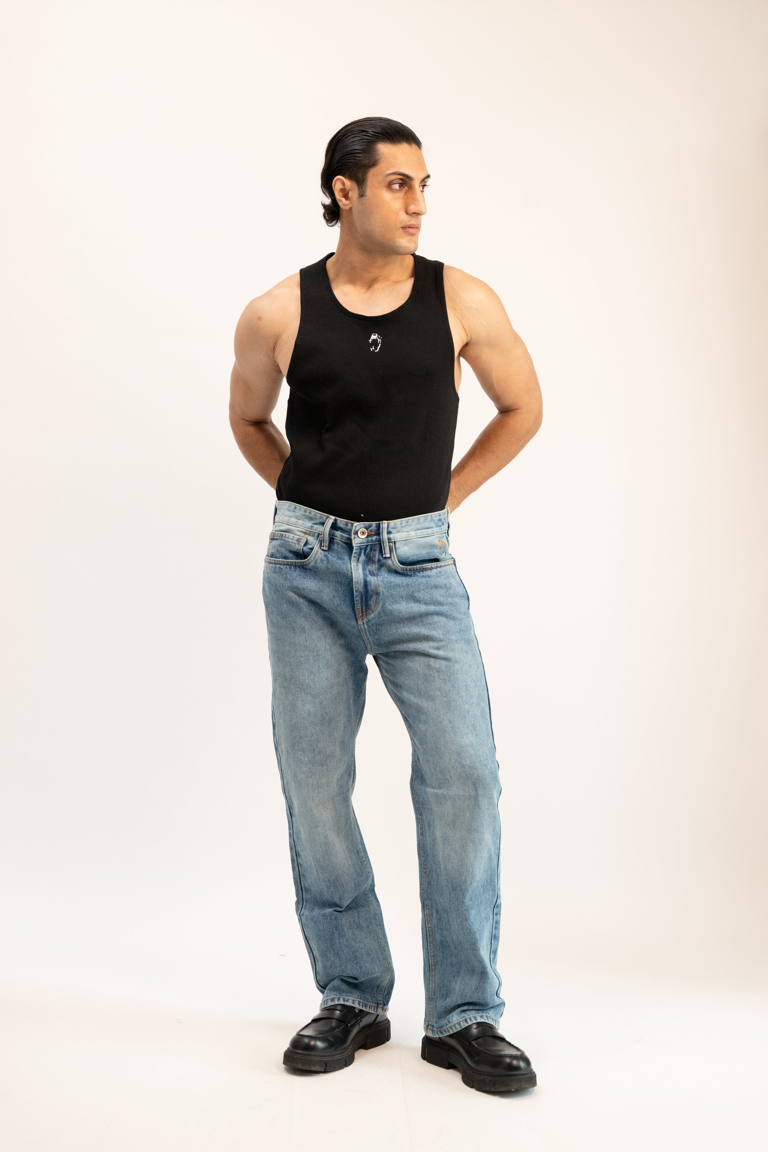 Man wearing a black tank top and blue jeans on a white background